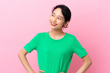Young Vietnamese woman isolated on pink background posing with arms at hip and smiling