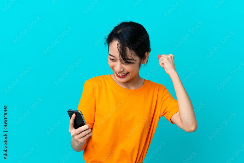 Wall mural Young Vietnamese woman isolated on blue background using mobile phone and doing victory gesture