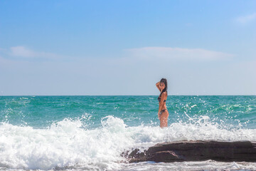 Fototapeta premium A beautiful emotional model girl splashes in the sea and laughs. Water splashes. Rest near the sea. The sea season.