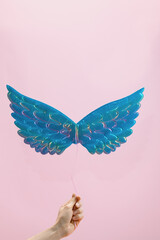 Levitate shiny holographic toy wings tied with a rope held in hand on a pink background. The...
