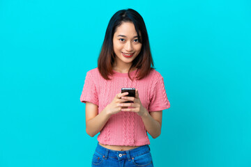 Young Vietnamese woman isolated on blue background sending a message with the mobile