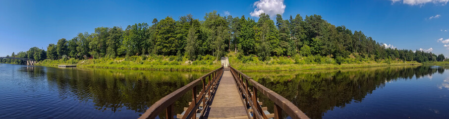 Fototapeta na wymiar view of the pontoon pedestrian bridge across the Gauja river, Ogre, Latvia.. Reflection of the forest in the water of the river. panoramic photo