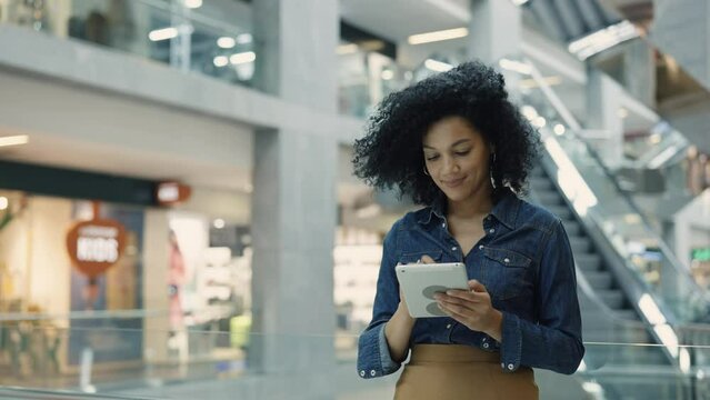 Happy african american woman texting using tablet and smiling. Shopping in a large modern center with branded clothing and goods. Shopping and fashion concept. Close up.