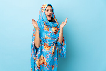 Young Moroccan woman with traditional costume isolated on blue background with surprise facial...
