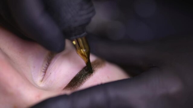 close-up of the tip of the tattoo machine and perform permanent eyebrow makeup on the girl model