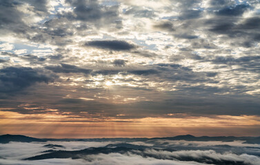 Fototapeta na wymiar Sunrise and cloudy sky over the mountains. The tops of the mountains in the fog. Cloud formation.