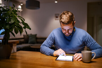 A man sitting at home, relaxing and scrolling on tablet.