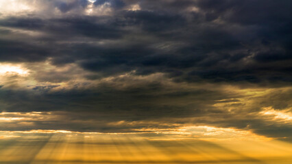 Sun beams or rays breaking through the dark clouds at sunset. Beautiful spectacular conceptual meditation background. Artistic golden sunset edit.