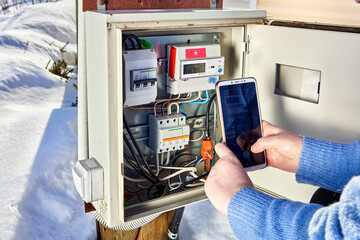 Taking readings from an electric meter in an outdoor electrical panel in winter, woman photographs...