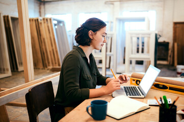 My business is as solid as the wood I work with. Shot of a female carpenter using a laptop in her...
