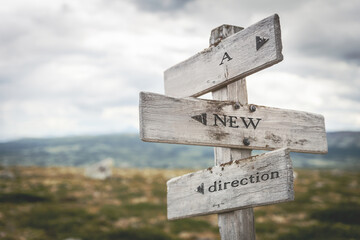 A new direction text quote written in wooden signpost outdoors in nature. Moody theme feeling.