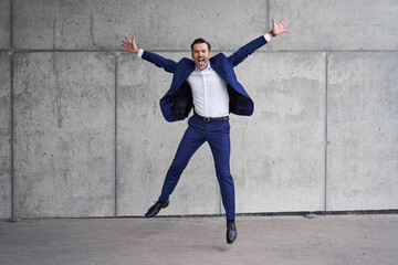 Successful businessman jumps against concrete wall with arms wide open
