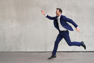 Picture of businessman in suit running against concrete wall
