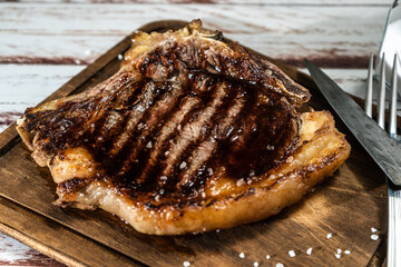 Incredible juice t-bone cooked on the grill or barbecue on a wooden board with cutlery on the side.
