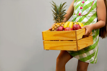 Niña cargando canasta de madera con rica y deliciosa fruta tropical hawaiana para disfrutar el...
