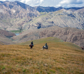 Fototapeta na wymiar Riders on horseback with weapons descend the mountain slope.