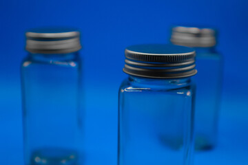 Blue background with glass containers in the foreground. Highly transparent with metal caps.