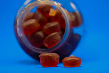 Plastic bottle full of gummy vitamins sideways with gummies falling out in front of blue background.