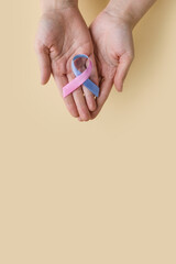 World Thyroid Day. Women 's hands hold Thyroid cancer awareness ribbon in Teal Pink Blue on beige background. Problems with thyroid. Polycystic disease. World cancer day.