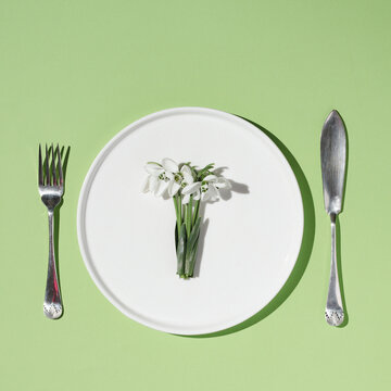 sunny spring plate with snowdrops and cutlery on a green background