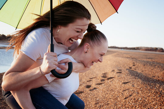 lesbian couple holding pride umbrella laughing at the beach