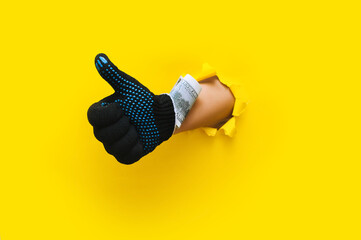 The right male hand in a black fabric work glove holds dollar bills (money) and shows a thumbs up...