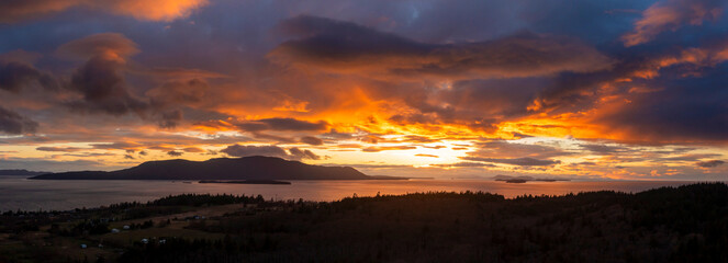 Aerial Panoramic View of Orcas Island During a Dramatic Sunset. Seen from neighboring Lummi island looking across Rosario Strait at the sun dropping below the dynamic cloudscape.