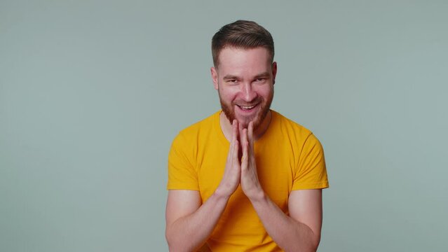 Sneaky cunning man with tricky face gesticulating and scheming evil plan, thinking over devious villain idea, cunning cheats, jokes and pranks. Young guy on gray studio wall background alone indoors