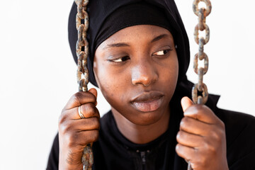 Sad young African girl behind the chains, symbolizing captivity, imprisonment or confinement; claim...