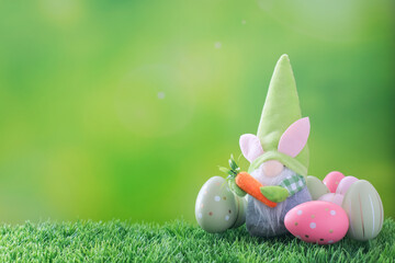 Easter composition on green. A cute garden gnome in a tall hat surrounded by decorated multi-colored Easter eggs on the grass. Spring green blurred background with copy space.