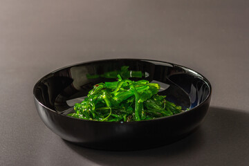 Wakame seaweed salad with sesame seeds and chili pepper in a bowl. Trendy hard light, dark shadow