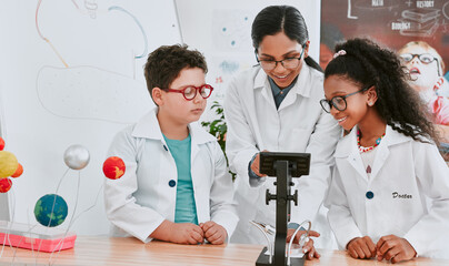 Lets take a closer look at this. Shot of a young science teacher using a microscope with her pupils in science class at school.