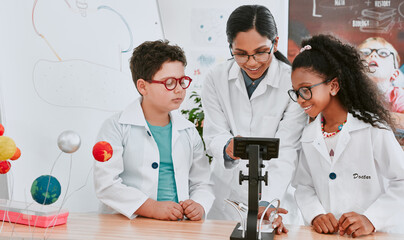 Lets take a closer look at this. Shot of a young science teacher using a microscope with her pupils...