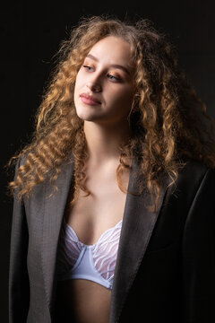 Portrait of a young red-haired curly sexy girl in a jacket with long hair in the studio. Shows off her curvaceous breasts in a bra.