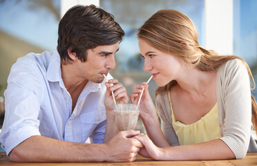 Sharing a milkshake. A young couple sharing a chocolate milkshake while on a date.