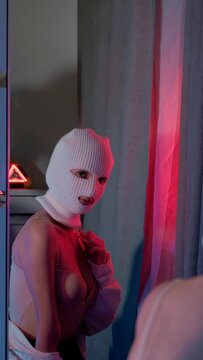 A girl in a white balaclava looks in the mirror. Close-up gangster admires himself. Sexy vertical video for a rap clip.