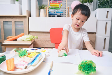 Homeschooling, Cute Asian kindergarten boy child making artwork from vegetable stamping at home,...