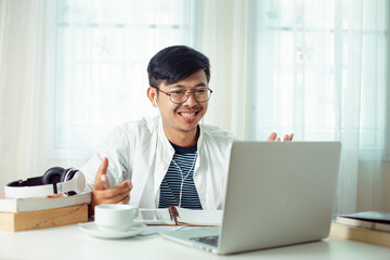 young Asian man video conference with a computer teacher in his home / concept E-learning, online education and internet social distancing protect from COVID-19 viruses.