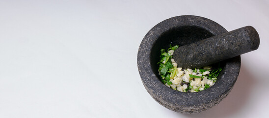 A mortar and pestle filled with fresh garlic, coriander, black peppercorns and salt to prepare a...