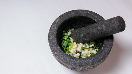 A mortar and pestle filled with fresh garlic, coriander, black peppercorns and salt to prepare a...