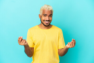 Young Colombian handsome man isolated on blue background making money gesture