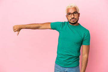 Fototapeta premium Young Colombian handsome man isolated on pink background showing thumb down with negative expression