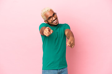 Young Colombian handsome man isolated on pink background pointing front with happy expression
