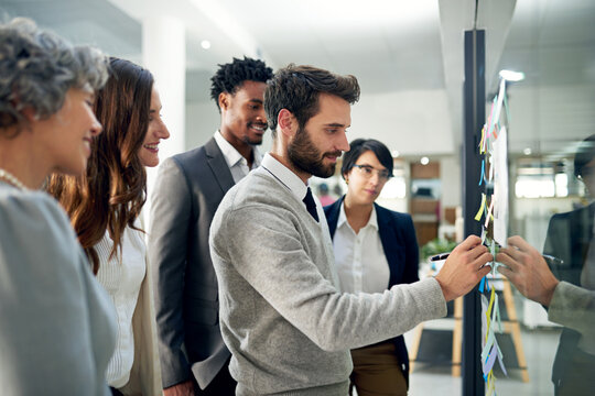 Heading Up The Planning Committee. Shot Of A Group Of Businesspeople Brainstorming On A Glass Wall In An Office.