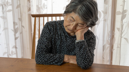 頬杖をつき何かに悩んでいる黒い服を着た高齢者女性