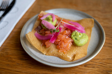 Mexican food, fried corn tortilla with smoked salmon, guacamole sauce and pink pickled onions