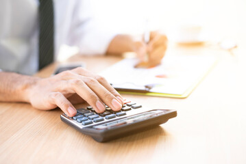 Close up with a businessman or accountant holding a pen to work on the calculator to calculate.