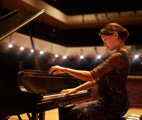 Hitting the right notes. Shot of a young woman playing the piano during a musical concert. - obrazy, fototapety, plakaty