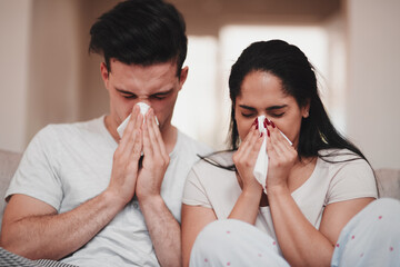 In sickness and health. Cropped shot of a young couple blowing their noses while sitting on the...