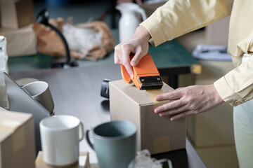 Closeup image of woman business owner working, packing the order for shipping to customer. Female entrepreneur packaging box for delivery in store warehouse.